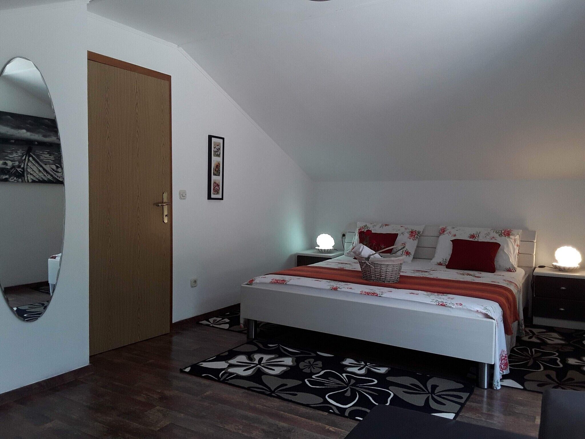 A bedroom with a bed, two bedside tables, a nightstand, a mirror, and a door.