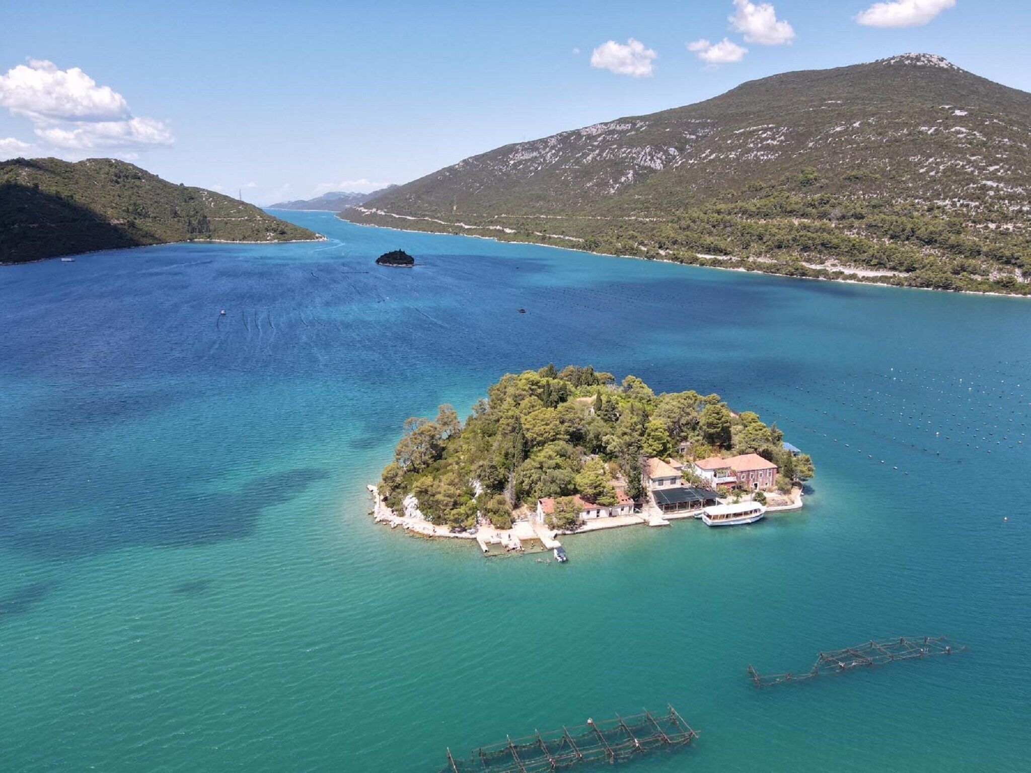 An aerial view of a small island with buildings, surrounded by clear blue waters and a mountainous landscape.