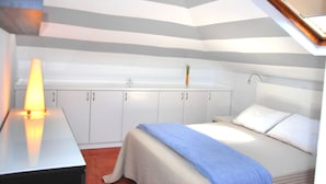 A bedroom with a bed, a bedside table with a lamp, white cabinets, and a sloped ceiling.