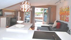 A modern kitchen with a dining area, a sofa with a red pillow, and a large window with a view of the outdoors.