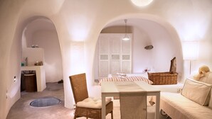 A cozy, well-lit room with a dining table, wicker chairs, a sofa, and a bed. - Santorini Finikia Oia Cave House (Santorini)