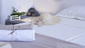 A neatly made bed with white linens, a crocheted hat, and a folded towel on a bedside table. - Santorini Finikia Oia Cave House (Santorini)