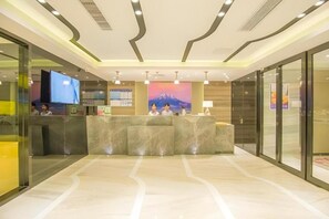 Ein Hotel-Rezeptionsbereich mit einem Marmor-Empfangstresen, einem großen Flachbildfernseher und einem Gemälde einer Berglandschaft an der Wand.