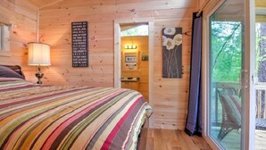 Une chambre dans une cabane en bois, avec un lit, un mur orné de citations inspirantes, une fenêtre donnant sur les arbres et une porte menant à la salle de bain.