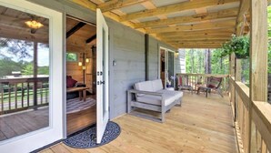 Une terrasse en bois avec un canapé et des fauteuils, une plante suspendue et une vue sur l’extérieur.