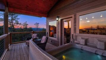 Terraza de madera con jacuzzi y zona de estar, con vistas a un paisaje pintoresco.