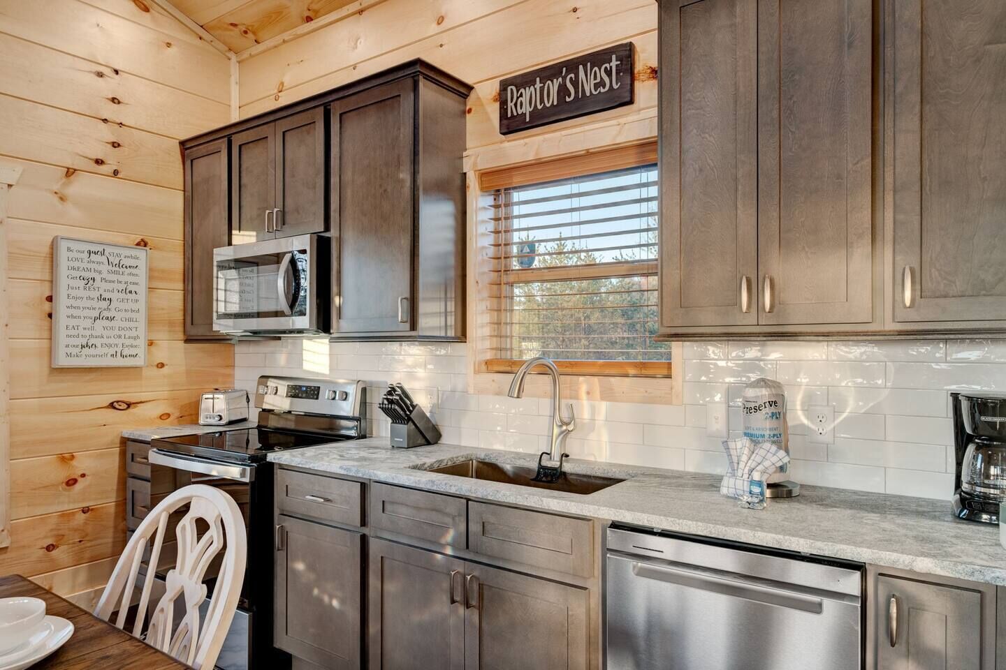 A modern kitchen with dark cabinets, stainless steel appliances, and a sign reading "Raptor's Nest".