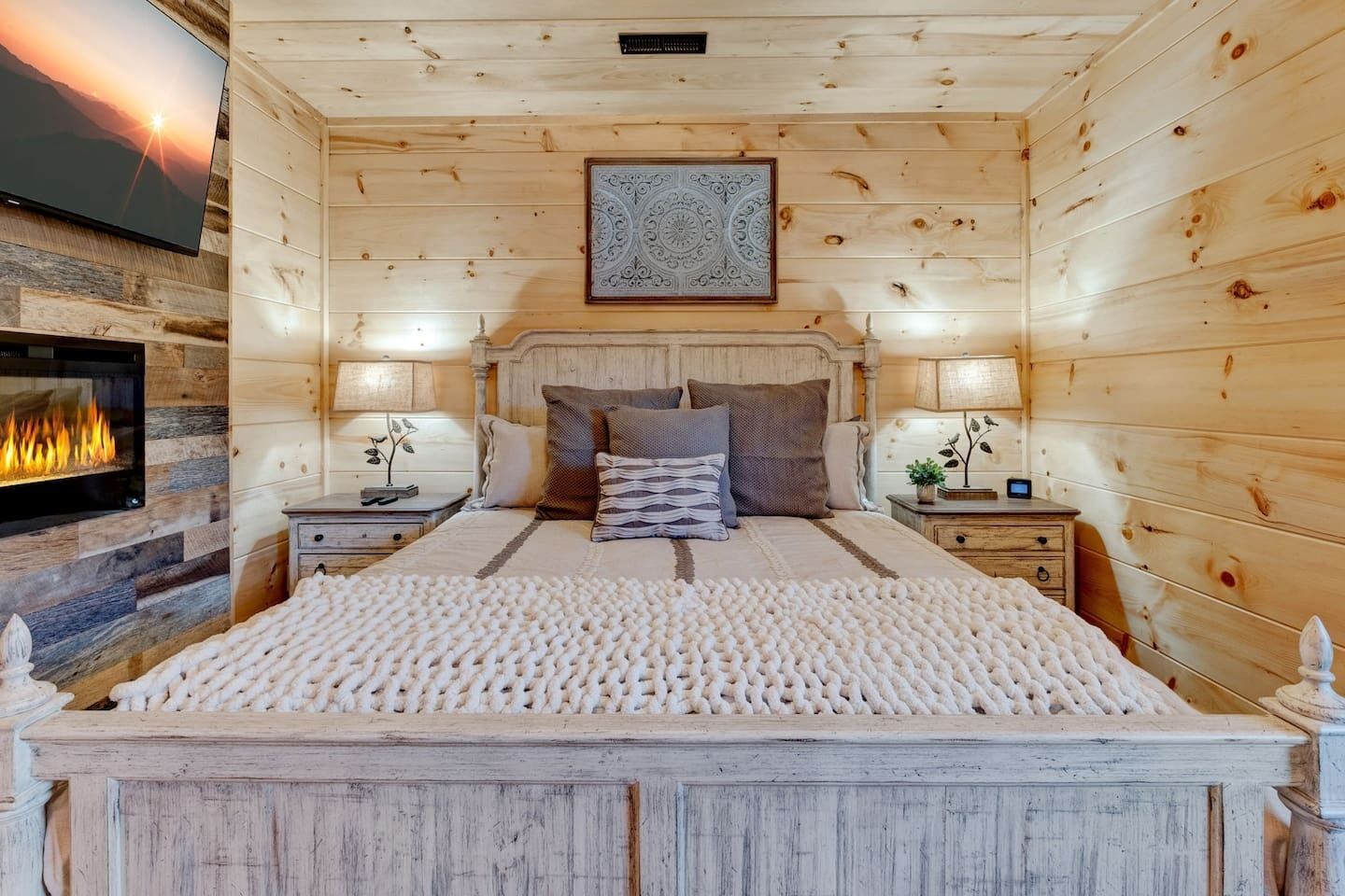 Une pièce chaleureuse aux murs de bois, comprenant un lit, des tables de chevet, une cheminée et un élément décoratif mural.