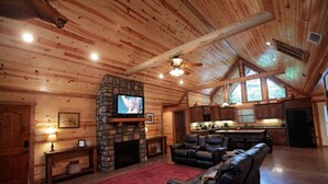 A spacious living room with a stone fireplace, leather seating, and a television. - 3BR Family Cabin in Hochatown with Hot Tub (Broken Bow)