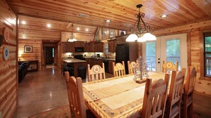 A wooden cabin interior with a dining area, kitchen, and a cozy living space. - 3BR Family Cabin in Hochatown with Hot Tub (Broken Bow)