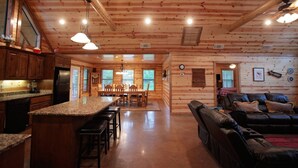 A spacious log cabin interior with a kitchen, dining area, and living room. - 3BR Family Cabin in Hochatown with Hot Tub (Broken Bow)
