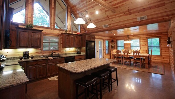 A spacious kitchen with granite countertops, wooden cabinets, and a central island with bar stools. - 3BR Family Cabin in Hochatown with Hot Tub (Broken Bow)