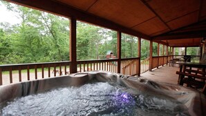 A hot tub area with a wooden deck, surrounded by trees. - 3BR Family Cabin in Hochatown with Hot Tub (Broken Bow)