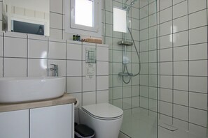 Casa de banho com lavatório, sanita e chuveiro brancos.
