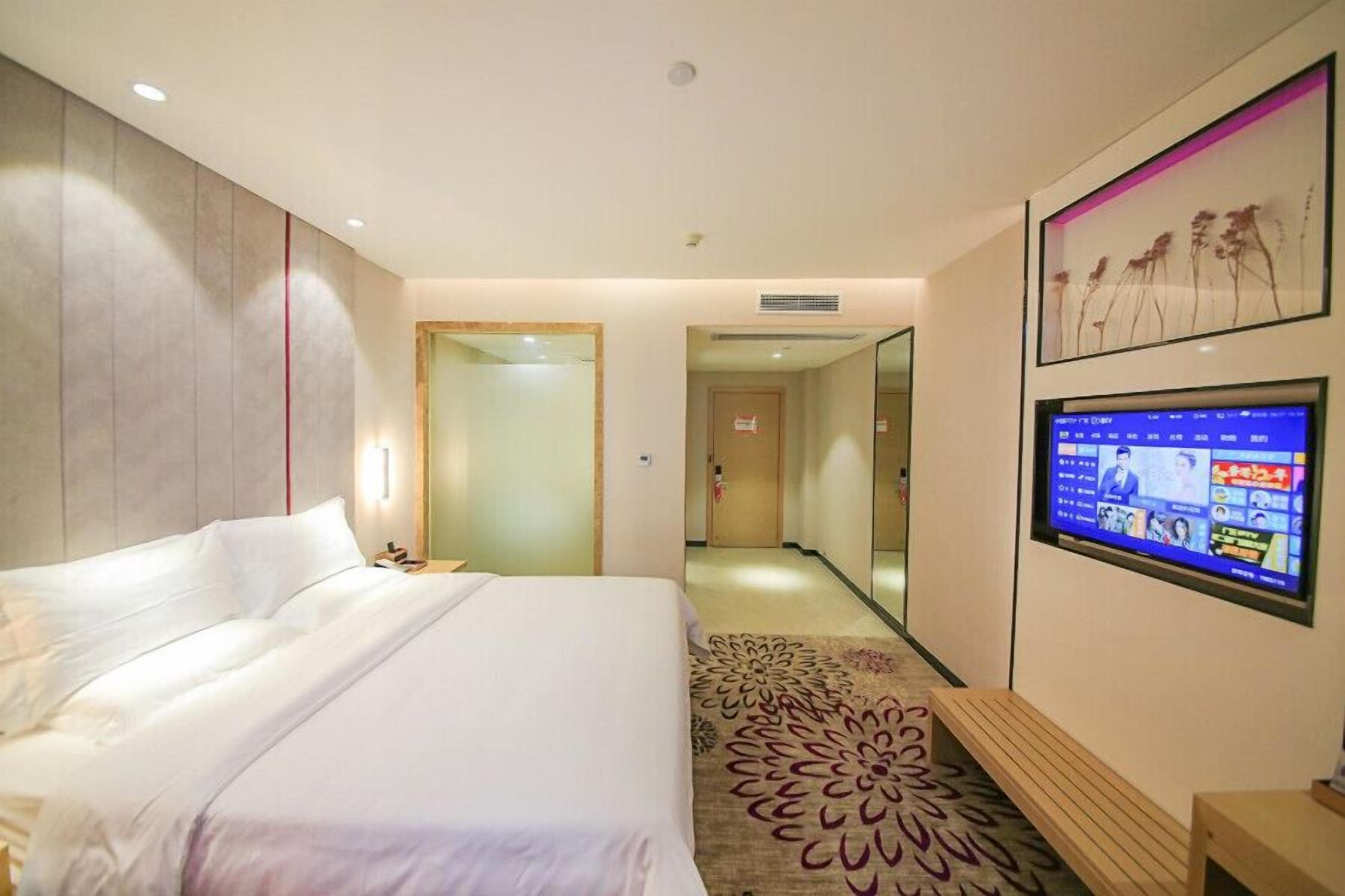Habitación de hotel con una cama grande, un televisor montado en la pared y una alfombra estampada con motivos florales.