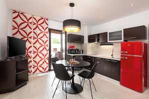 A modern kitchen with a dining table, chairs, a TV, and a red refrigerator.