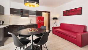 Una cocina moderna con armarios oscuros, un refrigerador rojo y un comedor con una mesa redonda y cuatro sillas.