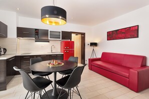 A modern kitchen with dark cabinetry, a red refrigerator, and a dining area with a round table and four chairs. - Apartment Urban 3 with balcony (Poreč)