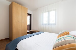 Ein Schlafzimmer mit einem Bett, einem Holzschrank, einer Bank und einem Fenster mit Vorhängen.