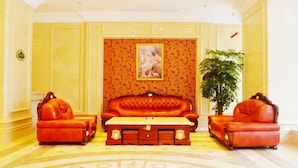 A room with a red sofa set, a wooden coffee table, and a large potted plant. - Vienna Hotel (Huizhou Zhongkai Chenjiang Avenue) (Huizhou)