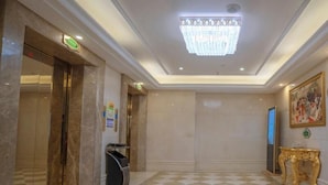 A hotel lobby with a checkered floor, a chandelier, a gold-framed painting, and a trash bin. - Vienna Hotel (Huizhou Zhongkai Chenjiang Avenue) (Huizhou)