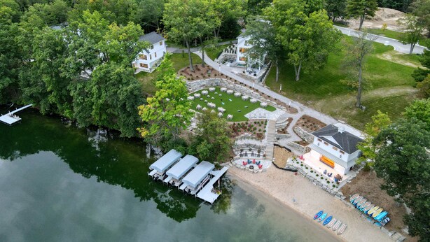 A lakeside property with a dock, outdoor seating, and a stone patio area. - Traverse City Lakemore Resort,  New Luxury Lakefront Home on Arbutus Lake (Traverse City)