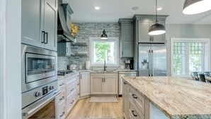 A modern kitchen with granite countertops, stainless steel appliances, and a large island. - Traverse City Lakemore Resort,  New Luxury Lakefront Home on Arbutus Lake (Traverse City)