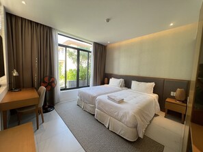 A hotel room with two beds, a desk, a chair, a fan, and a window with curtains. - Suite & Pavilion Thien Kim (Cam Lam)