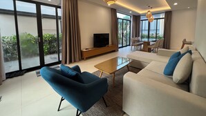 A modern living room with a sofa, armchair, TV, and dining area. - Suite & Pavilion Thien Kim (Cam Lam)