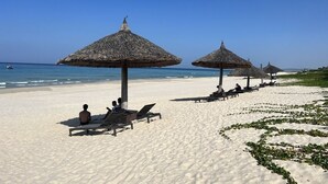 A beach with thatched umbrellas and lounge chairs, a clear sky, and the ocean in the background. - Suite & Pavilion Thien Kim (Cam Lam)