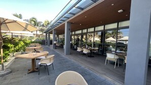 An outdoor patio area with wooden tables and wicker chairs, large umbrellas, and a view of the ocean. - Suite & Pavilion Thien Kim (Cam Lam)