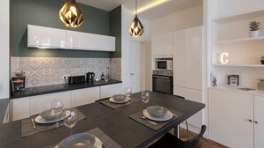 A modern kitchen with a dark countertop, white cabinets, and two pendant lights. - Le Confident - Grand T2 au coeur de Lyon (Lyon)