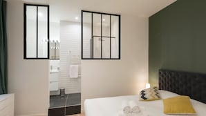 A hotel room with a bed, a nightstand, a mirror, a bathroom with a shower, and a green accent wall. - Le Confident - Grand T2 au coeur de Lyon (Lyon)