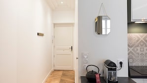 A hallway with a wooden floor, a white door, a wall-mounted mirror, a kettle, and a coffee machine. - Le Confident - Grand T2 au coeur de Lyon (Lyon)