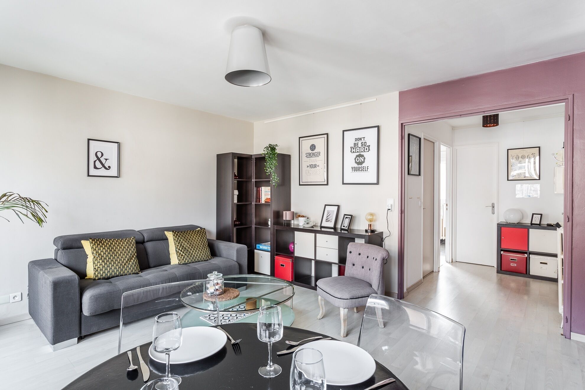 Una sala moderna con un sofá, una mesa de centro de vidrio y un comedor con sillas y una mesa preparada para dos personas.