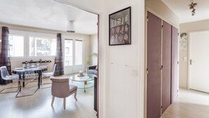A modern living room with a dining area, featuring a glass coffee table, a round dining table with chairs, and a large window with curtains. - LORGERIL - appartement 2 chambres proche du Mail (Rennes)