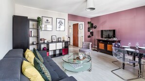 A modern living room with a sofa, coffee table, and a dining area with chairs and a TV. - LORGERIL - appartement 2 chambres proche du Mail (Rennes)