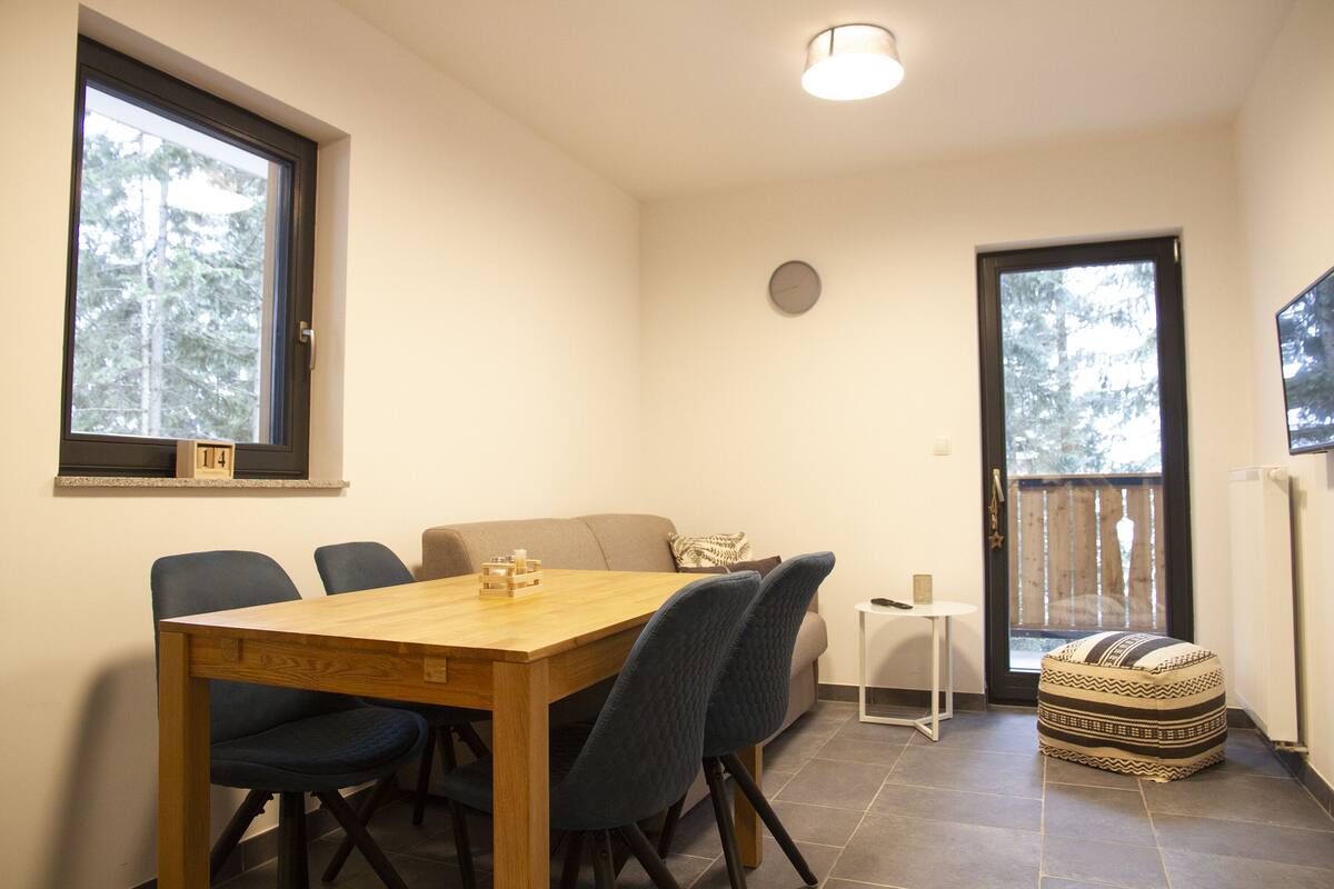 A dining area with a wooden table and chairs, a small side table, and a sofa.