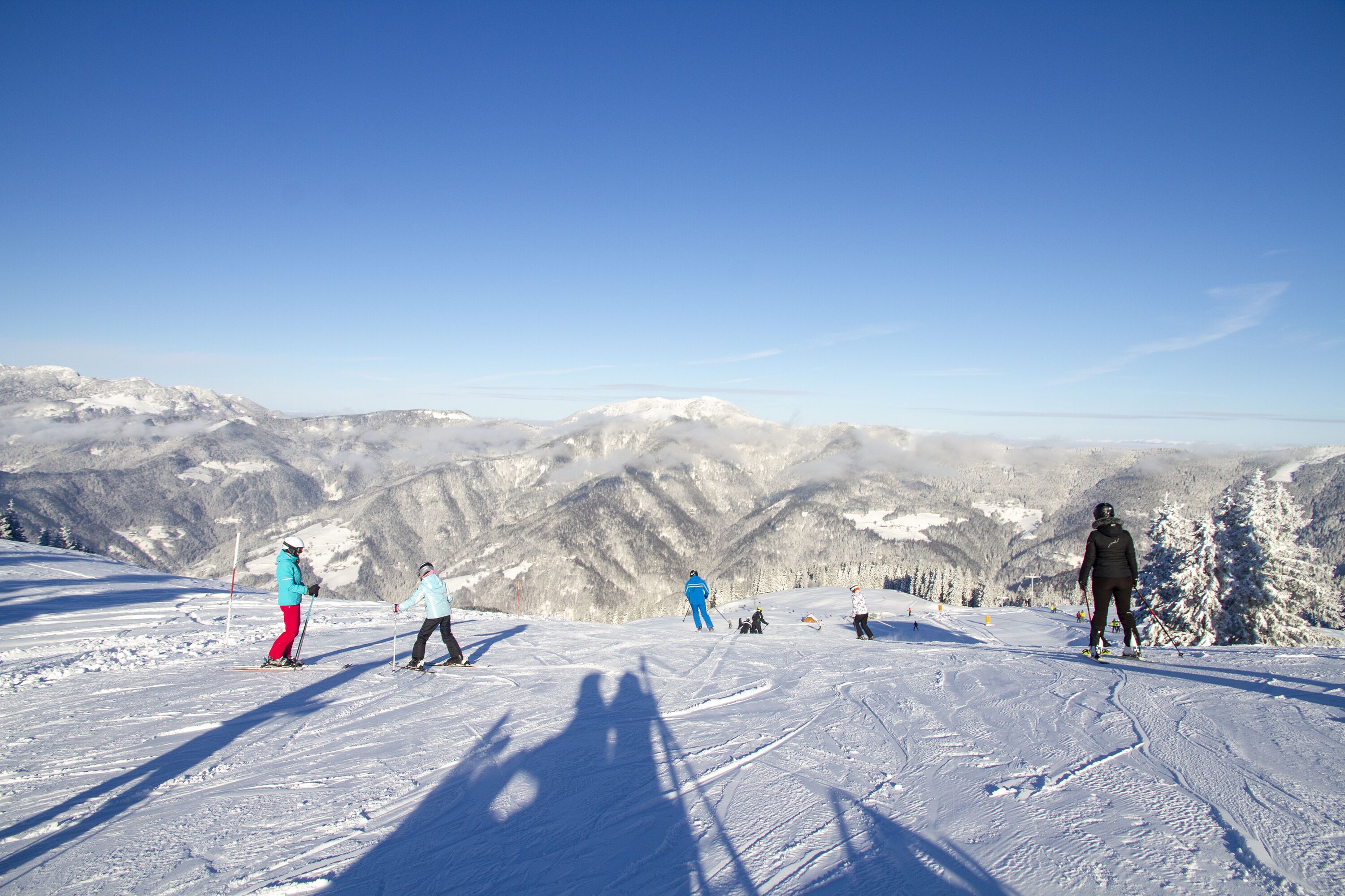 Ein verschneiter Skipisten mit Skifahrern und freiem Blick auf die umliegenden Berge.
