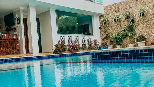 Una piscina con borde de azulejos, un balcón con barandilla de cristal y plantas en macetas.