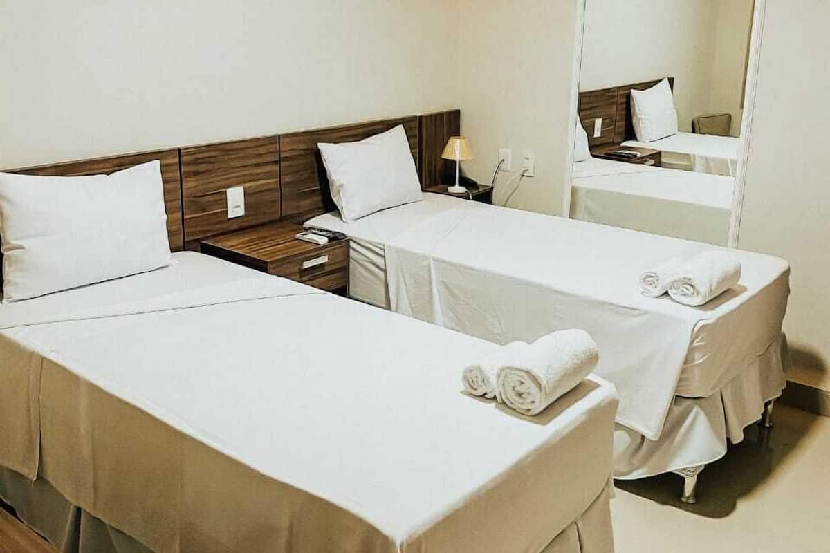 Une chambre d’hôtel avec deux lits simples, une table de chevet avec une lampe, un miroir et un petit coin salon.