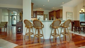 A spacious kitchen with wooden cabinets, a central island with bar stools, and a dining area with chairs. - 3rd row updated home in Palmetto Dunes Resort, large private pool & hot tub (Hilton Head Island)