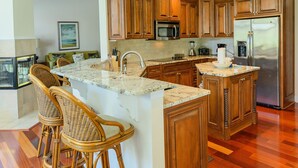 A spacious kitchen with wooden cabinets, a large island with bar stools, a stainless steel refrigerator, and a microwave. - 3rd row updated home in Palmetto Dunes Resort, large private pool & hot tub (Hilton Head Island)