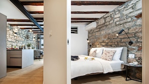A bedroom with a stone wall, a bed with pillows, a bedside table, and a lamp. - Dal Pescatore Apartment in the Old Town (Rovinj)
