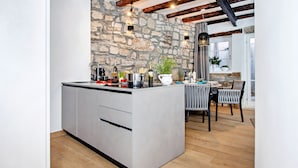 A modern kitchen with a stone wall, a central island, and a dining area with a table and chairs. - Dal Pescatore Apartment in the Old Town (Rovinj)