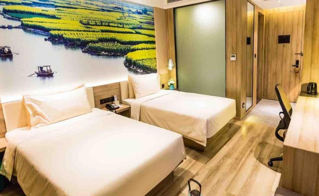 A hotel room with two beds, a desk, a chair, and a large mural of a river landscape.