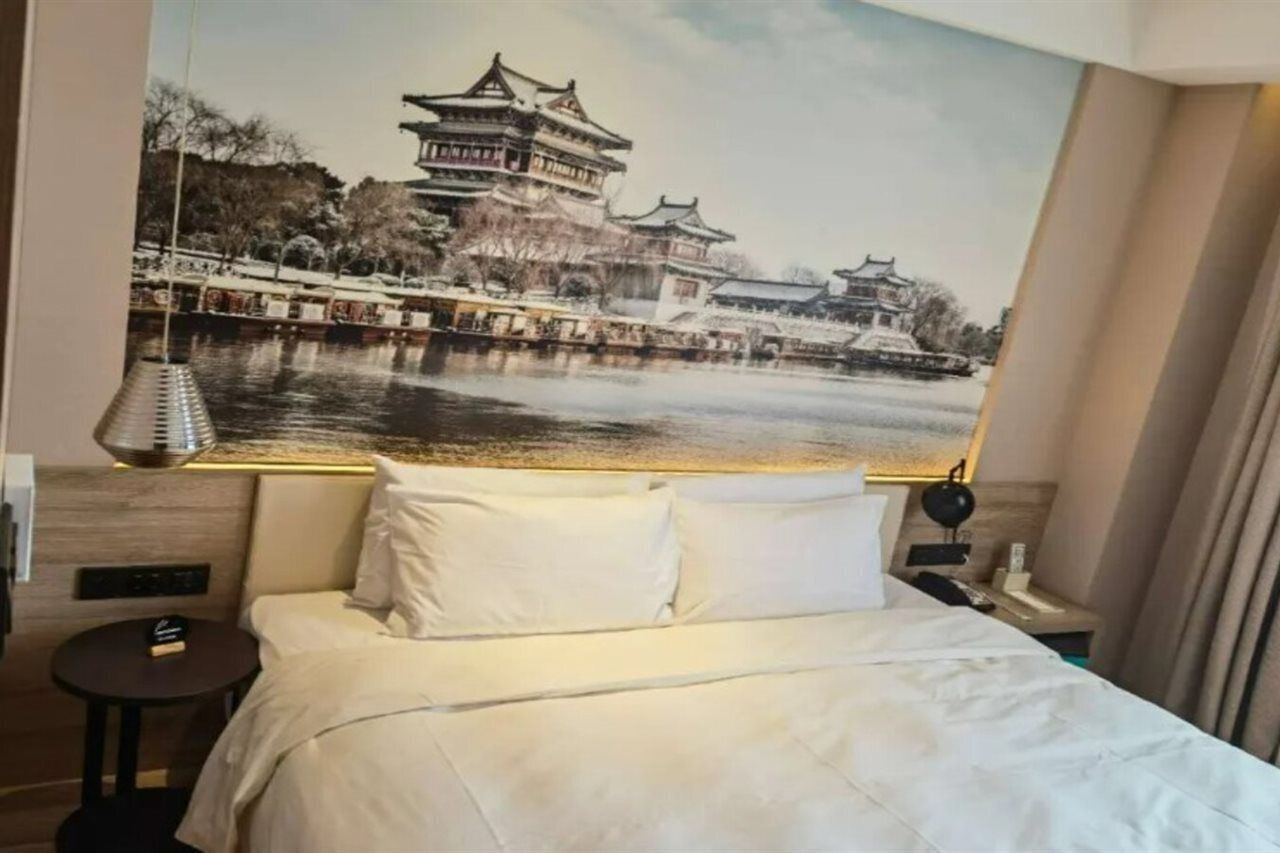 A hotel room with a large bed, a small bedside table, a lamp, and a wall-mounted TV.