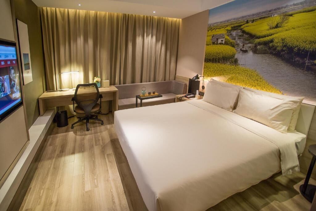 Habitación de hotel con una cama grande, un escritorio con silla, una mesita con lámpara y un ventanal con vistas a un río y campos.