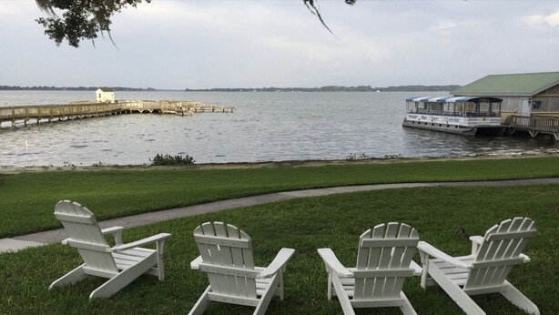 A waterfront view with a dock, a boat, and a grassy area with Adirondack chairs. - Dora Splash Pad (Mount Dora)