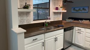 A modern kitchen with white cabinets, a granite countertop, a stainless steel sink, and a window with a view. - Dora Splash Pad (Mount Dora)